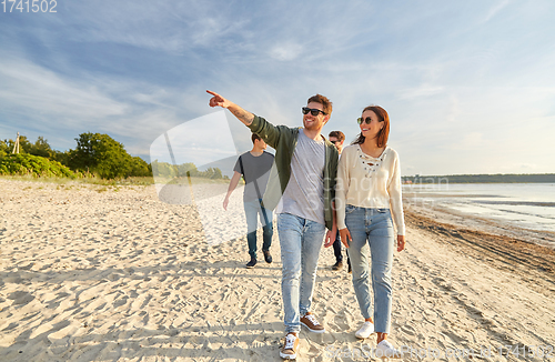 Image of happy friends walking along summer beach