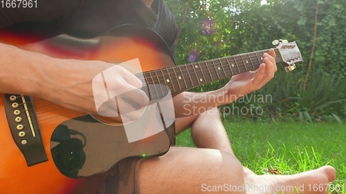 Image of Man sitting in the grass playing guitar