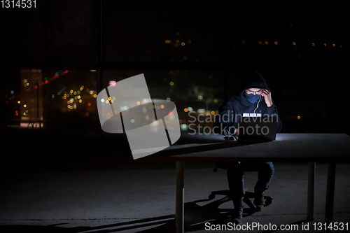 Image of hacker using laptop computer while working in dark office