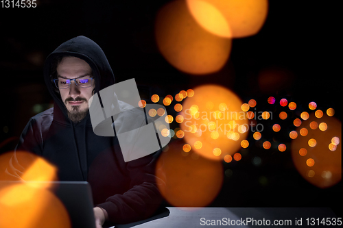 Image of hacker using laptop computer while working in dark office