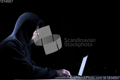 Image of hacker using laptop computer while working in dark office