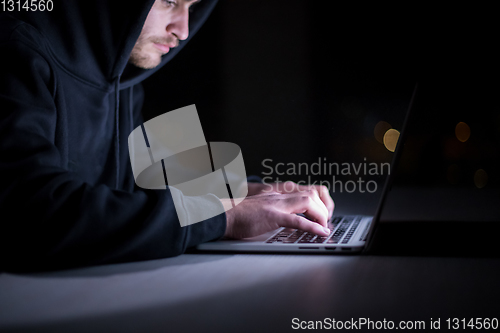 Image of hacker using laptop computer while working in dark office