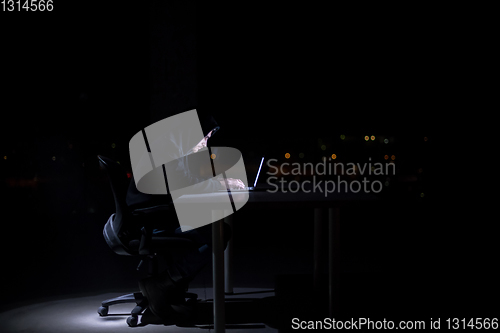 Image of hacker using laptop computer while working in dark office