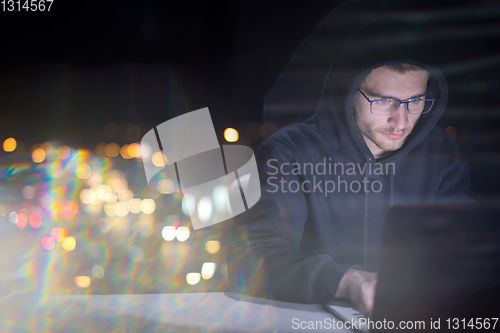 Image of hacker using laptop computer while working in dark office