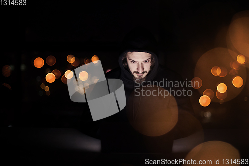 Image of hacker using laptop computer while working in dark office