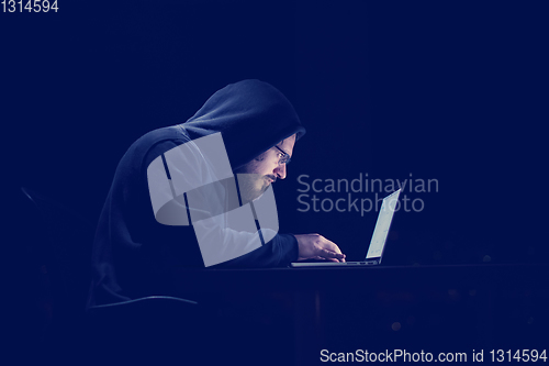 Image of hacker using laptop computer while working in dark office