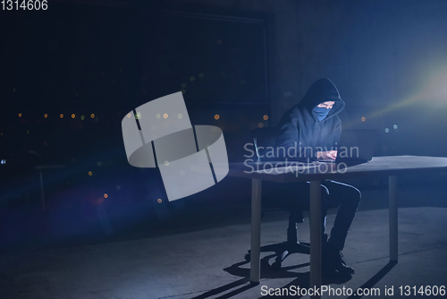 Image of hacker using laptop computer while working in dark office