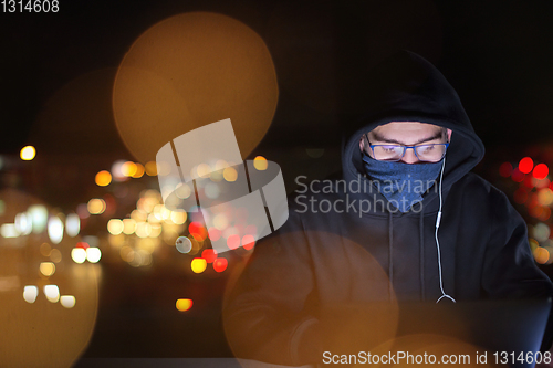 Image of hacker using laptop computer while working in dark office