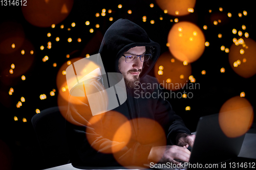 Image of hacker using laptop computer while working in dark office