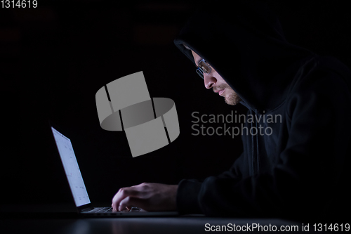 Image of hacker using laptop computer while working in dark office