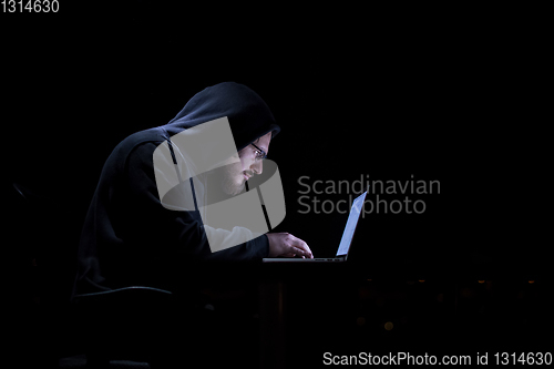 Image of hacker using laptop computer while working in dark office