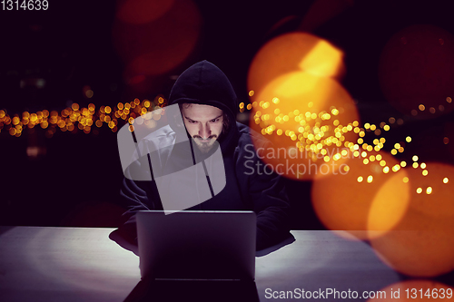 Image of hacker using laptop computer while working in dark office