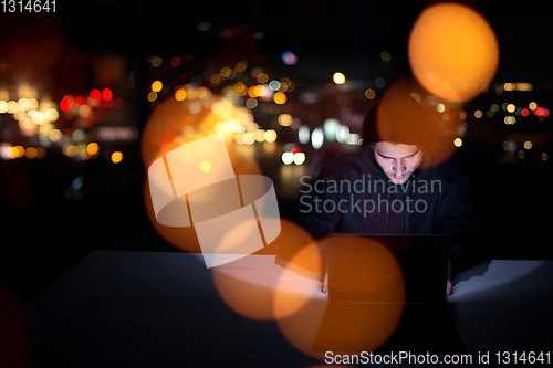 Image of hacker using laptop computer while working in dark office