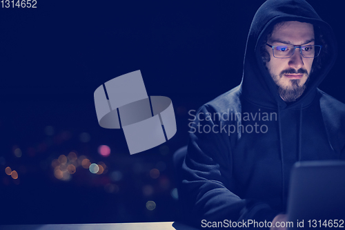 Image of hacker using laptop computer while working in dark office