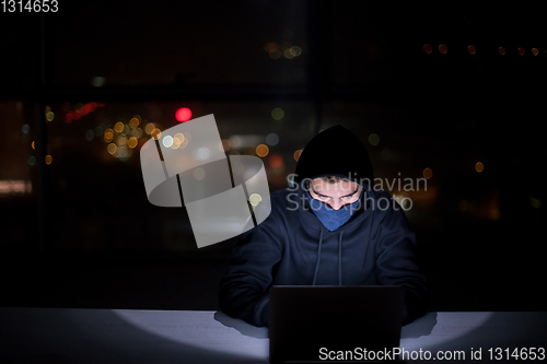 Image of hacker using laptop computer while working in dark office