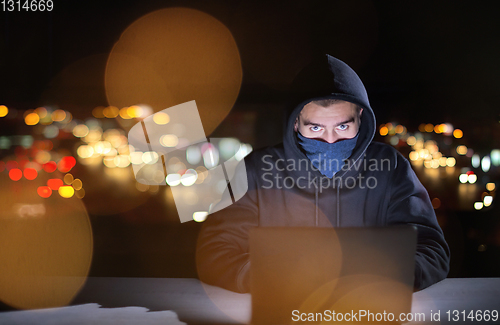 Image of hacker using laptop computer while working in dark office