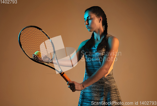 Image of One caucasian woman playing tennis on brown background in mixed light