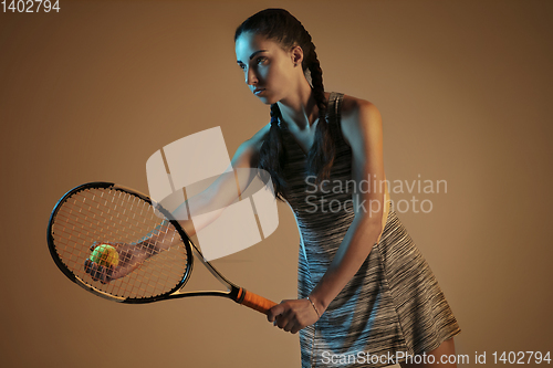 Image of One caucasian woman playing tennis on brown background in mixed light