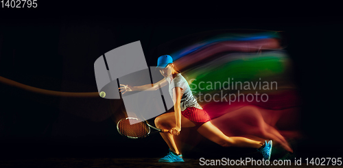 Image of One caucasian woman playing tennis on black background in mixed light