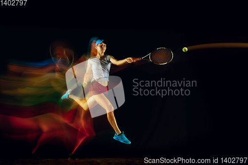 Image of One caucasian woman playing tennis on black background in mixed light