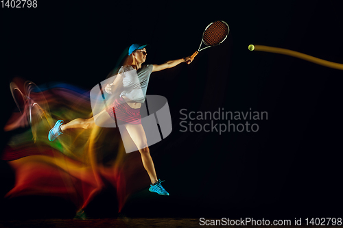 Image of One caucasian woman playing tennis on black background in mixed light