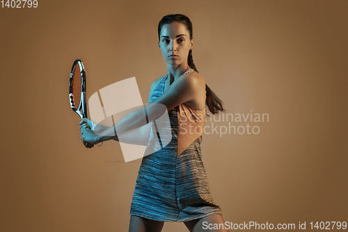 Image of One caucasian woman playing tennis on brown background in mixed light