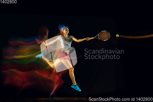 Image of One caucasian woman playing tennis on black background in mixed light