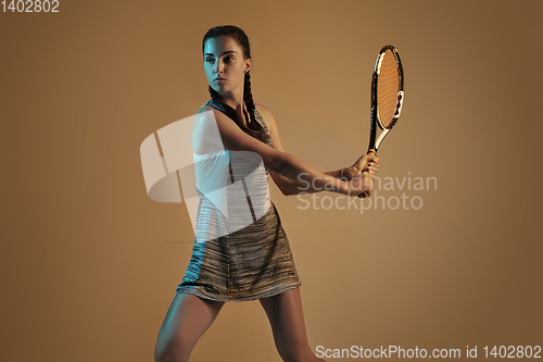 Image of One caucasian woman playing tennis on brown background in mixed light