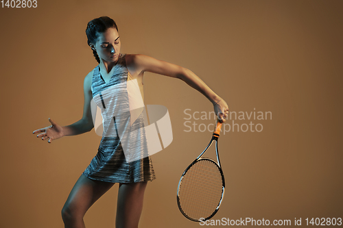 Image of One caucasian woman playing tennis on brown background in mixed light