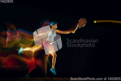 Image of One caucasian woman playing tennis on black background in mixed light