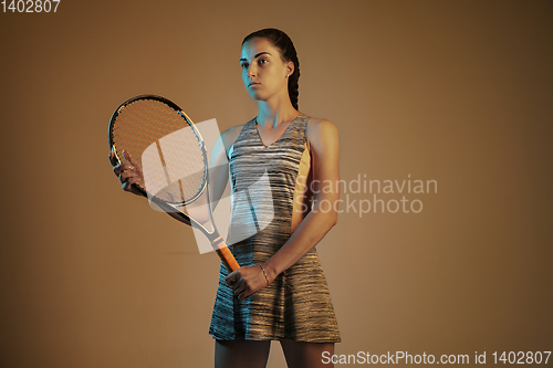 Image of One caucasian woman playing tennis on brown background in mixed light