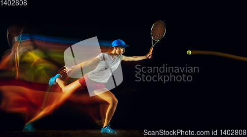 Image of One caucasian woman playing tennis on black background in mixed light