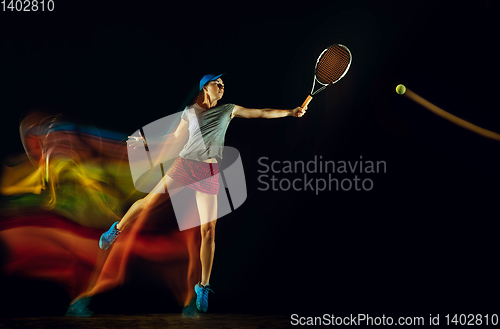 Image of One caucasian woman playing tennis on black background in mixed light