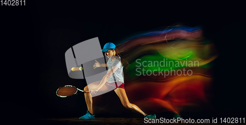 Image of One caucasian woman playing tennis on black background in mixed light