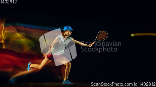 Image of One caucasian woman playing tennis on black background in mixed light