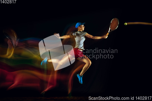 Image of One caucasian woman playing tennis on black background in mixed light