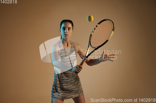 Image of One caucasian woman playing tennis on brown background in mixed light