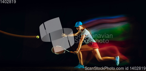 Image of One caucasian woman playing tennis on black background in mixed light