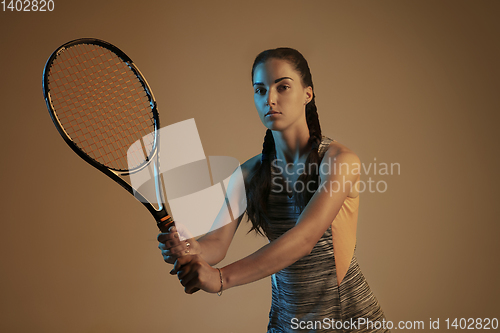 Image of One caucasian woman playing tennis on brown background in mixed light
