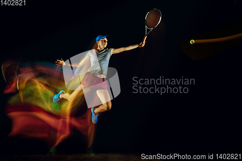 Image of One caucasian woman playing tennis on black background in mixed light