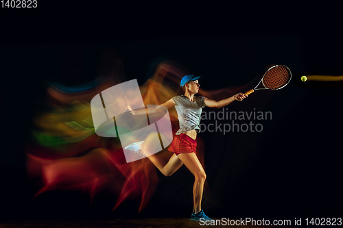 Image of One caucasian woman playing tennis on black background in mixed light