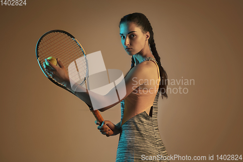 Image of One caucasian woman playing tennis on brown background in mixed light