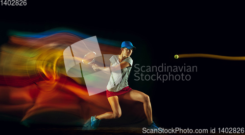 Image of One caucasian woman playing tennis on black background in mixed light