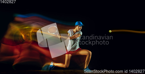 Image of One caucasian woman playing tennis on black background in mixed light