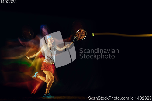 Image of One caucasian woman playing tennis on black background in mixed light