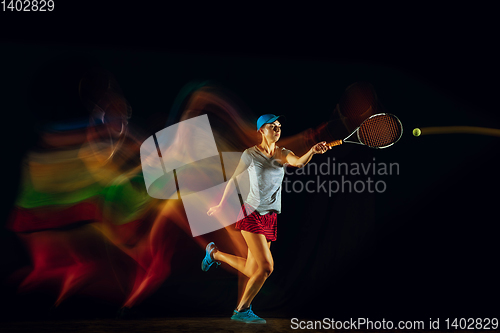 Image of One caucasian woman playing tennis on black background in mixed light