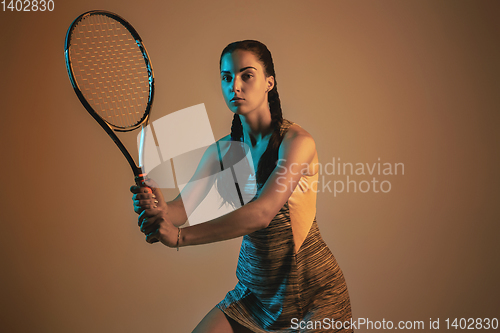 Image of One caucasian woman playing tennis on brown background in mixed light