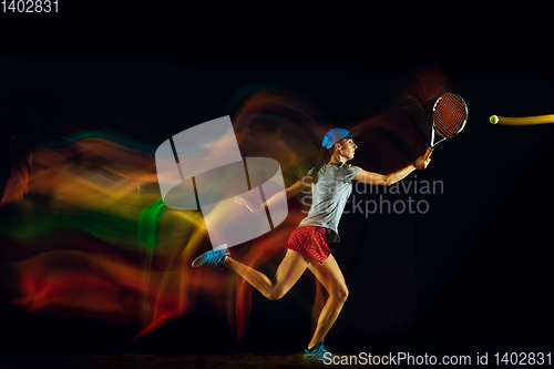 Image of One caucasian woman playing tennis on black background in mixed light