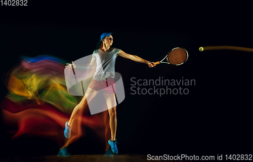 Image of One caucasian woman playing tennis on black background in mixed light