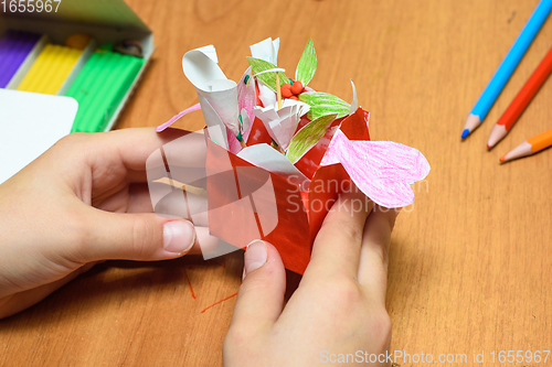Image of A girl holding a homemade gift for mom in her hands, stationery on the table in the background